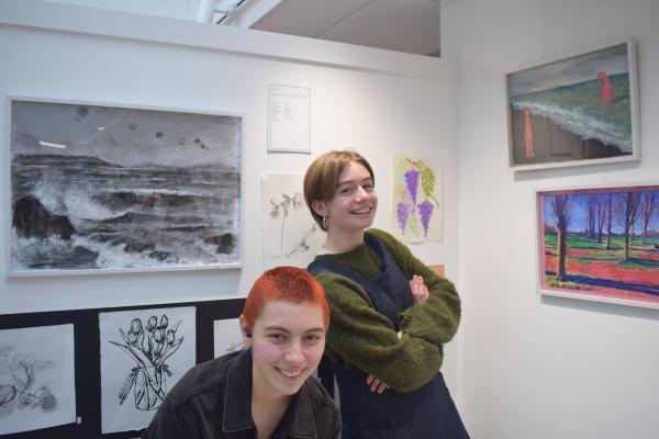 Two students stand in front of displayed work